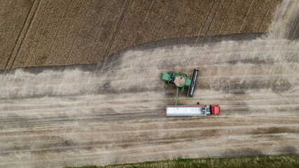 Aerial view with harvester dumping crop into a truck trailer