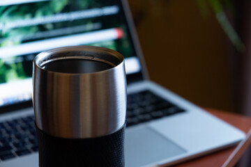metal thermo mug with a hot drink on the background of a laptop