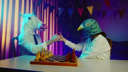 A young man and a woman in pigeon and unicorn masks are fighting with their thumbs. Multicolored lighting. Masquerade