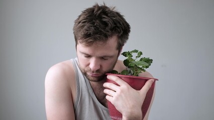 Drunk stressed man sitting hugging a pot with flower being alone.