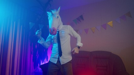 A young man in a unicorn mask is dancing. Multicolored lighting. Masquerade