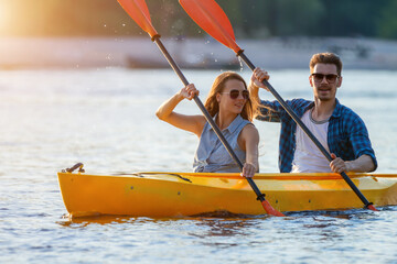 Confident young caucasian couple kayaking on river together with sunset in the backgrounds. Having fun in leisure activity. Romantic and happy woman and man on the kayak boat. Sport, relations concept