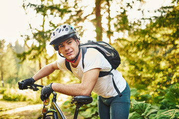 Naklejka premium Tired bicyclist in sport clothes and helmet taking break after outdoors training. Healthy caucasian man spending free time for workout on fresh air.