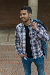 Obraz premium high angle shot of a nice-looking guy with hispanic features with one hand carrying his jacket over his shoulder and the other on his pocket while looking something smiling