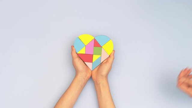 World autism awareness day concept. Woman and child hands holding puzzle heart on light blue background. Top view