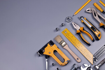 Working tools background. Screwdriver, tape measure, wrench, knife, pliers, pencils, ruler, pliers, metal screws, and other accessories on grey background. Repair and construction concept 