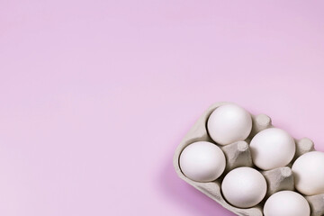 Fresh chicken eggs in egg carton box on pink background. Top view, flat lay with copy space. Natural healthy and organic food concept.