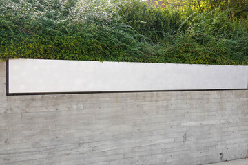 Long white blank sign on a stone wall with bushes above it