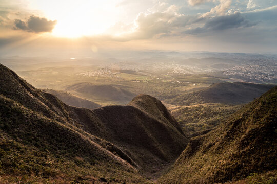 Deep valley between the mountains and the cities of Brumadinho and Ibirite in the background at dusk.