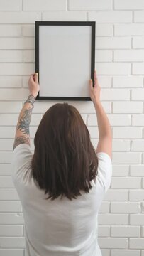 a girl hangs an empty frame on a white brick wall