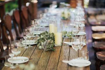 Elegant wooden table for wedding outdoor in garden, in the style of rustic with eucalyptus and candles, porcelain plates, glasses.