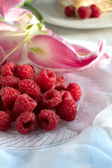 delicious raspberries on plate with lily flower on background. Antioxidant for healthy living 