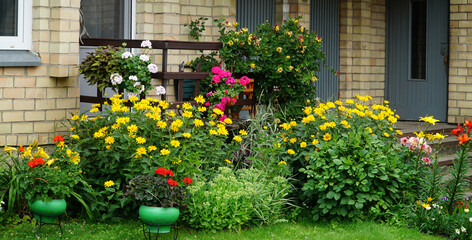 Fototapeta na wymiar The porch of small house in rural style surrounded by perennial and annual colorful flowers in summer.