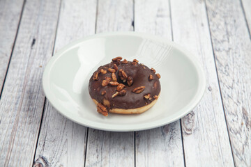 Chocolate donuts with hazel nuts on a white plate on Wood table 