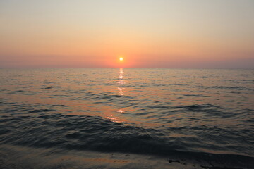 Fototapeta premium Sunset over the sea. Calm sea on a summer evening at sunset on the coast of Calabria, holidays at sea in Italy