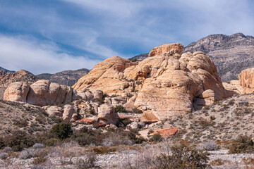 Las Vegas, Nevada, USA - February 23, 2010: Red Rock Canyon Conservation Area. Group of beige boulders under blue cloudscape. Gray mountain on horizon and dry desert floor with bushes up front.