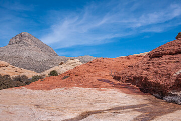 Fototapeta premium Las Vegas, Nevada, USA - February 23, 2010: Red Rock Canyon Conservation Area. Red rock dominates over beige with wet line under blue cloudscape. Gray mountain top on horizon.