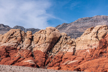 Fototapeta na wymiar Las Vegas, Nevada, USA - February 23, 2010: Red Rock Canyon Conservation Area. Beige rocky layer on top of red layer on mountains in front of snow capped gray mountain under blue cloudscape.