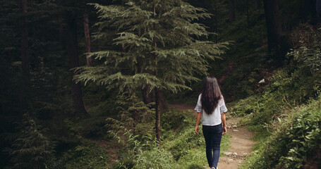 Back view of a young brunette Indian girl walking through the forest full of lush green trees