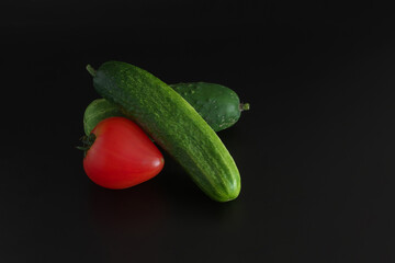 Two cucumbers and a red tomato on a black background. Copy space.
