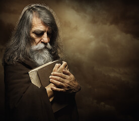 Praying Monk with Bible. Prophet holding Book. Old Man Portrait with Long Gray Beard in Black Cloak...