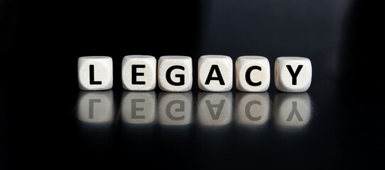 The inscription JEGACY on wooden cubes isolated on a dark background, the concept of business and finance.