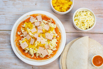 Artisan pizza before baking, with cheese, ham, pineapple, pomodoro sauce, accompanied by flavors