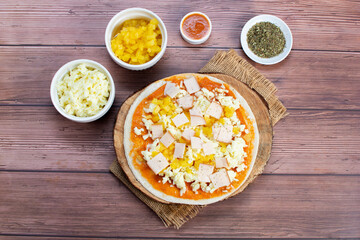 Artisan pizza before baking, with cheese, ham, pineapple, pomodoro sauce, accompanied by flavors