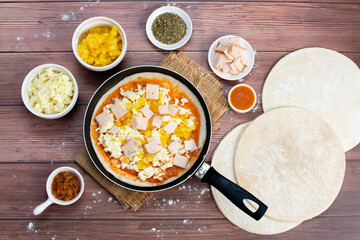 Artisan pizza before baking, with cheese, ham, pineapple, pomodoro sauce, accompanied by flavors