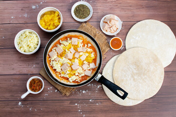 Artisan pizza before baking, with cheese, ham, pineapple, pomodoro sauce, accompanied by flavors
