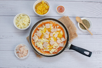 Artisan pizza before baking, with cheese, ham, pineapple, pomodoro sauce, accompanied by flavors