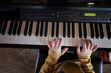 Young child practicing playing a piano with hands resting on keys