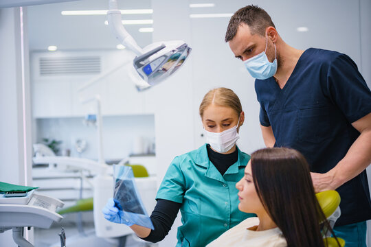Two dentists examine and repair the patient's teeth. They use X-ray image. Three people in the dental office.