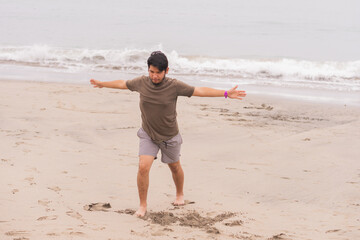 Young Hispanic man practicing various poses in yoga on the beach