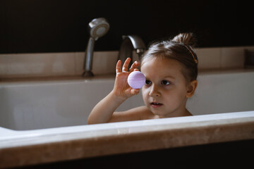 Child holding bath bomb. Relaxing hygiene procedure for kids. Aromatherapy and fun at home. Happy toddler girl in bathtub washing herself