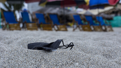Face mask is being left on the beach and buried in the sand: pollution of face mask in nature,...