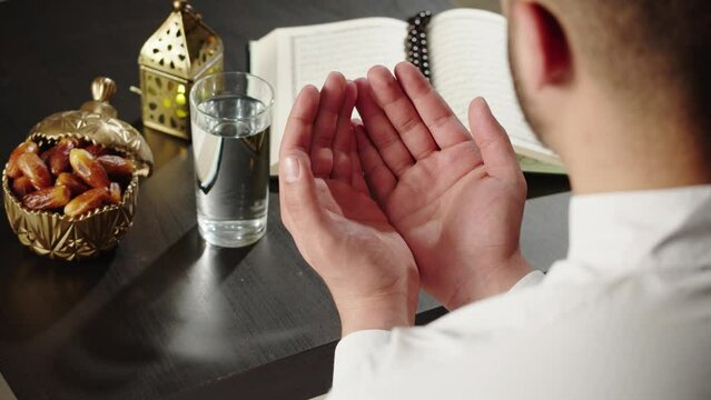 Man praying close-up, dua, islamic religion. Religious holiday Ramadan, holy month. Muslim worship, egyptian making traditional prayer to God, namaz. Eating dates with water. 