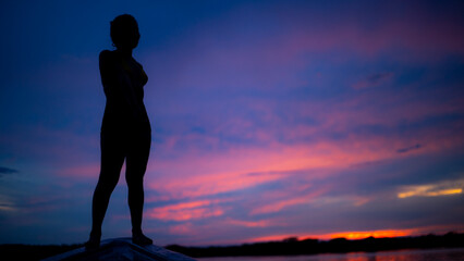 A woman posing at the front of a canoa during sunset while on holiday