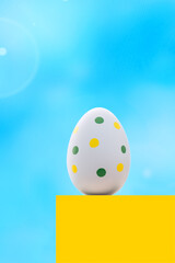 A blue spotted Easter egg on a yellow pedestal against the blue sky. Conceptual Easter card in the colors of the Ukrainian flag with copy space.