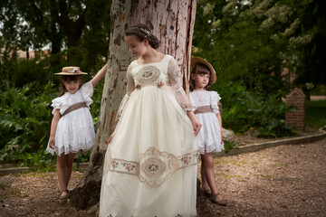 Communion girl posing with her twin little sisters in a park