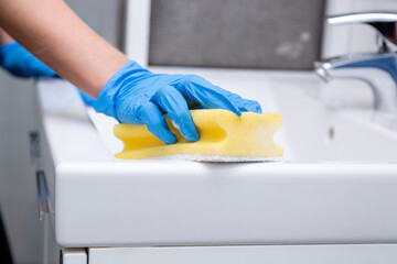 Hand with blue glove cleaning a sink with a yellow sponge