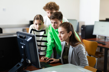 Female teacher helping schoolboy and schoolgirl in computer class