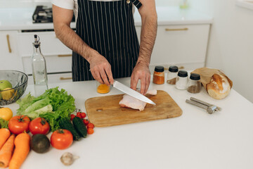 Products for cooking on the kitchen table. A man cuts a chicken on a board