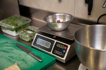 balanza pesar carne picada en bol metalico en interior cocina restaurante con brotes, tabla de cortar verde, cuchillo metalico close-up