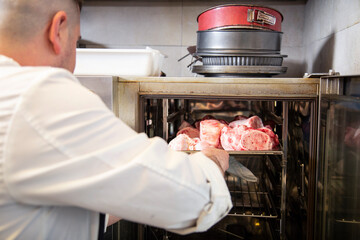 chef manos introduce bandeja con carne cruda en horno con uniforme blanco en interior de cocina de...