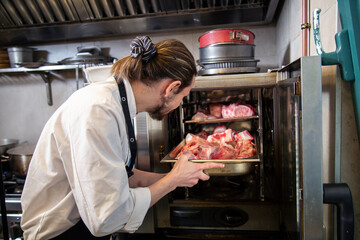 chef manos introduce bandeja con carne cruda en horno con uniforme blanco en interior de cocina de...