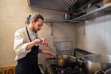 chef cuece tortelini pasta fresca con salsa tradicional y queso en cocina de restaurante italiano