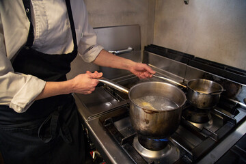 chef manos cocina en olla pasta fresca tortellini en interior cocina restaurante con uniforme blanco y mandil negro