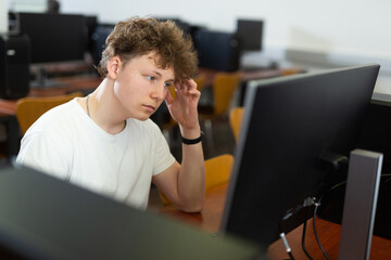 Tired schoolboy with a sore head sits at a computer in the classroom