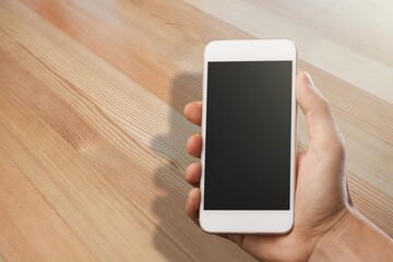 Human holding a smartphone on the screen. Rustic wooden table.tic wooden table. Rio de Janeiro, RJ, Brazil. January 2022.